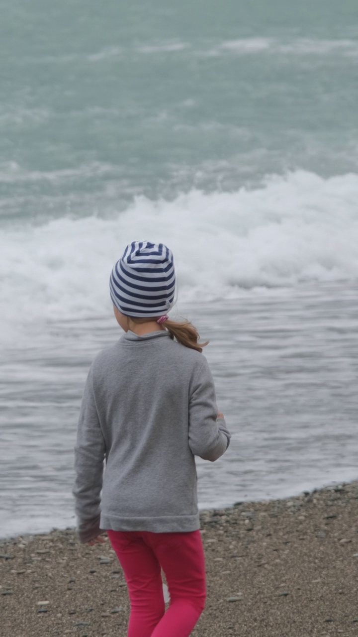 一个小女孩在波涛汹涌的大海上行走的背影