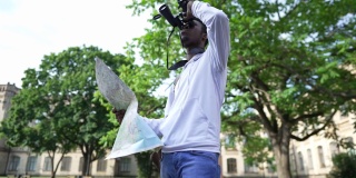 专注的非洲裔美国男性游客用双筒望远镜查看纸质地图。青年集中精神出国旅行，选择前进方向的人像。旅游和生活方式。