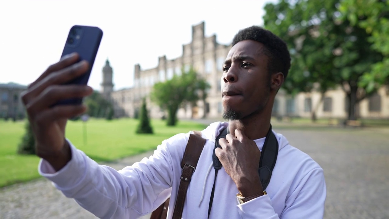 一名年轻的非洲裔美国人站在大学院子外面自拍。自信的男学生在大学校园拍照。生活方式与教育理念。