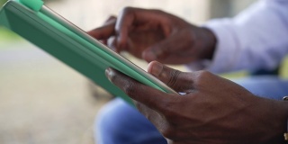 近距离拍摄的非洲裔美国男性用平板电脑上网聊天。一个面目全非的年轻人坐在户外使用app。现代科技和便利理念。