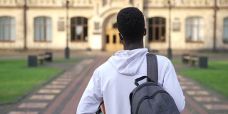 后视镜，自信的年轻学生步行到大学校园的慢镜头户外。一个聪明的非裔美国人，在春秋的一天，拿着书去上大学。教育智慧。