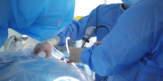 一组医生给病人做手术。外科医生穿着医用制服，戴着口罩在手术室里工作。