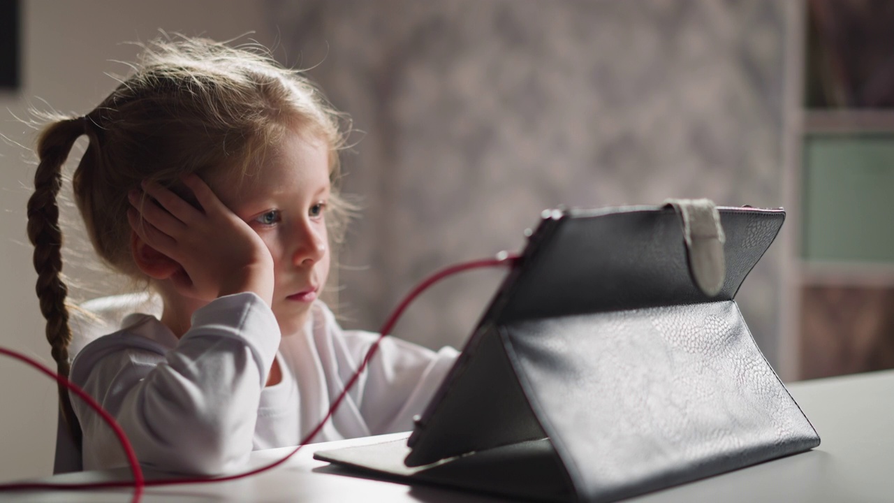 无聊的女孩在桌子上通过平板电脑看教育视频