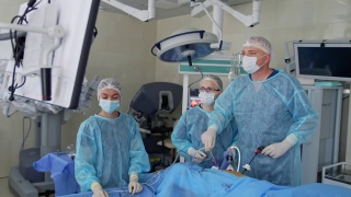 主刀外科医生在手术中使用医疗设备，看着显示器显示病人的内部器官。两名医生协助主刀外科医生。技术在外科手术中的应用。视频素材模板下载