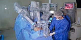 外科医生在机械臂的帮助下进行手术。帮助外科医生的女助手。屏幕显示手术的位置在背景。