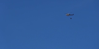 一架载着水箱的直升机在正午的蓝天上飞行