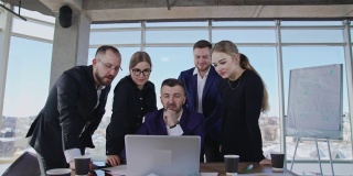 同事们围着坐在笔记本电脑前的老板。头脑风暴小组合作和讨论在电脑上。