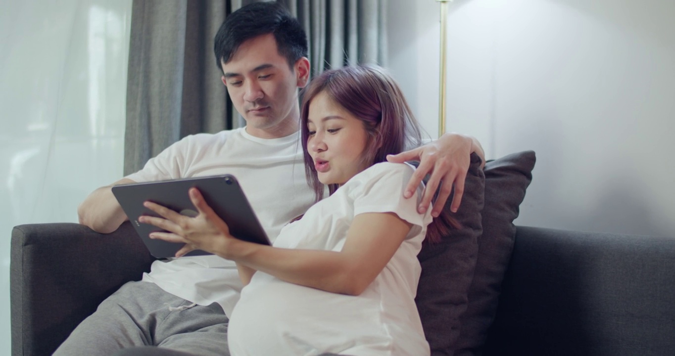 快乐的白人丈夫和怀孕的妻子在平板电脑上看她刚出生的孩子的超声波照片。