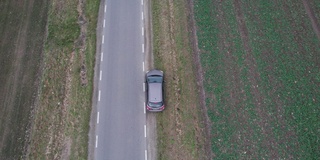 汽车正行驶在穿过田野的道路上，无人机拍下了鸟瞰图。秋天的时候在柏油路上，镜头跟着车走。