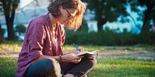 一个年轻的女人坐在公园的草坪上，在她的笔记本上做笔记。