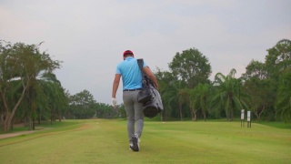 一名亚洲男子高尔夫球手步行和携带高尔夫球袋在高尔夫俱乐部视频素材模板下载