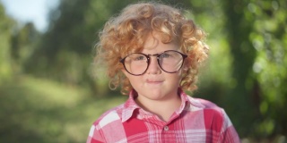 可爱的红发小男孩戴着眼镜，在阳光明媚的春夏季公园户外摆姿势。自信聪明的白人快乐的孩子看着镜头微笑的肖像。情报和休闲。