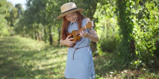在春天的公园里，一个红发少女站在阳光下，穿着蓝色的衣服，戴着草帽，弹着四弦琴。有才华的自信的高加索青少年享受户外爱好的肖像。