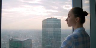 透过摩天大楼的窗户看城市风景的沉思的女人