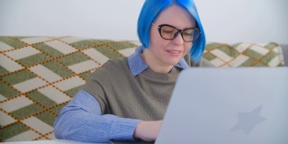 专注的年轻女子在电脑上打字。美丽的女性染成蓝色的头发工作在家里的4k股票视频剪辑笔记本电脑。千禧一代在笔记本电脑和互联网上做远程自由职业