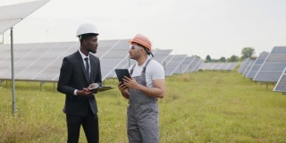 非裔美国检查员手里拿着平板电脑给印度技术人员讲解太阳能工厂的工作。生态工程和替代能源概念。和技术人员谈论太阳能电池板