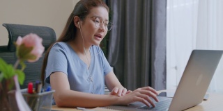 亚洲自由职业妇女戴着耳机在视频电话聊天在家里工作。
