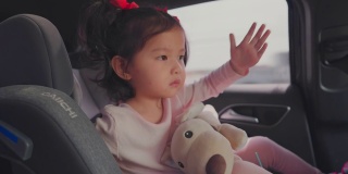 蹒跚学步的小女孩在汽车座椅上唱歌跳舞。