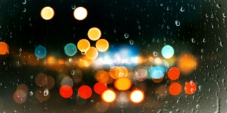 雨点落在玻璃窗上，映衬着城市背景的绚丽多彩的散景灯光效果。