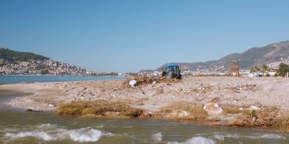 带铲斗的拖拉机在暴风雨后收集和清除沙滩上的垃圾和碎片。浑浊的河水流入大海