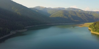 鸟瞰大湖，清澈湛蓝的湖水在茂密的常绿森林覆盖的高山之间。