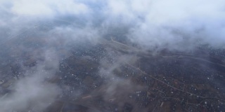 从高空俯瞰，在暴雨来临之前，蓬松的积云覆盖着遥远的城市。多云天气的飞机视角