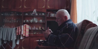 拿着智能手机的老人坐在扶手椅上浏览社交媒体。