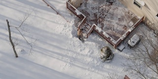 一个成年人在冬天下雪后用铲子清理门廊上的积雪。鸟瞰图直接在无人机视频上方。