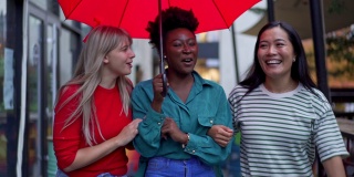 一个欢快的城市，多种族的女性朋友走在伞下的雨天在城市
