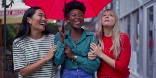 一个现代都市多种族女性朋友的肖像在雨天行走在城市的伞下