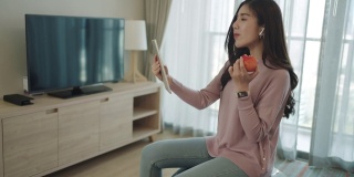 在家里工作的时候，一名亚洲女性在瑜伽球上放松、吃东西、在数码平板电脑上与同事们在线聊天。