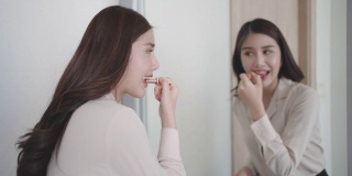 美丽的亚洲妇女穿着红色的衣服把口红看在镜子里她的卧室在家里。早上化妆，上班前准备。