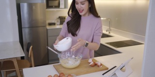 亚洲女性在家里厨房用数码平板电脑在线学习烘焙课程。