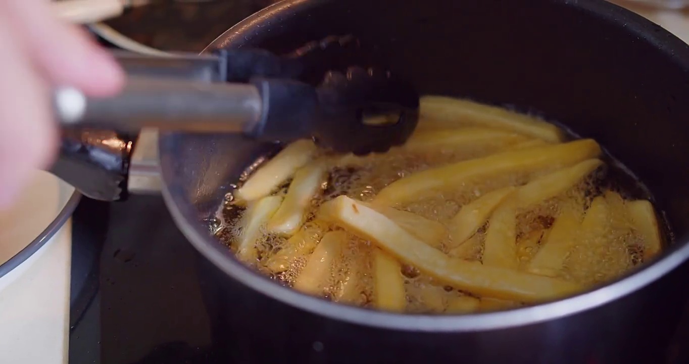在厨房，快餐店里，用钳子在滚烫的油里炸炸自制的黄色薯条和土豆