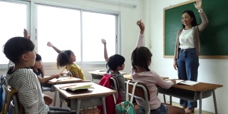 一群小学生拿着笔记本坐在教室里，举手回答老师的问题。教育，小学，学习，回到学校的概念
