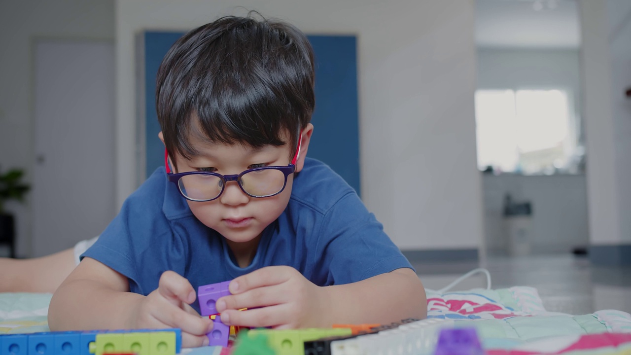 人像吸引人的聪明可爱的快乐的亚洲小男孩戴着眼镜享受在客厅玩五颜六色的高楼