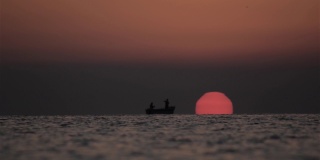 当一轮红彤彤的太阳浮出水面时，渔夫们在海上撒网