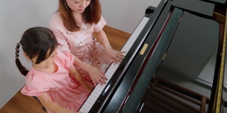 钢琴家在学校的教室里教一个女孩弹钢琴。最喜欢的古典音乐。在学习中快乐和乐趣。身着正装的音乐家。教育、练习、放松的理念。