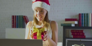圣诞夜办公室里一个戴着圣诞帽的年轻女人。她在一次网络视频通话中收到了一份礼物，并感谢了她的男友