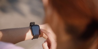 年轻的女运动员在公园跑步的后视图，同时使用智能手表检查她自己
