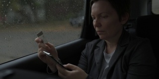 女商人在雨中坐在汽车后座使用信用卡和智能手机进行电子银行
