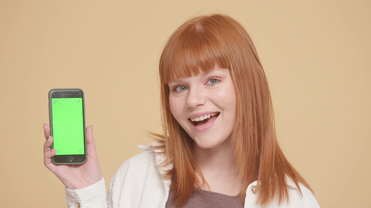 红发白人女性展示智能手机与绿色屏幕的色度键
