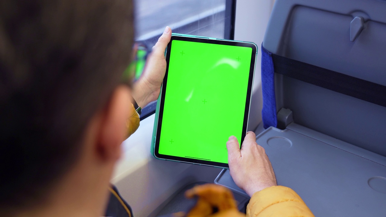 后视图男子观看平板电脑与绿色屏幕和浏览在线列车。模拟在pad上观看内容。坐在公共交通室内的男子手里拿着空白的数字电话