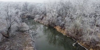 冬天无人机在河边飞行，河边的树木和灌木上结着白霜和雾凇