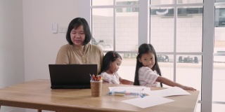 亚洲妇女视频通话笔记本电脑，同时照顾她的女儿在家里