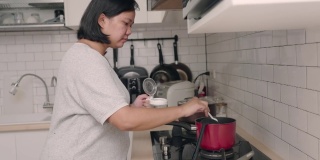 亚洲妇女在厨房做饭，同时看平板电脑的食谱