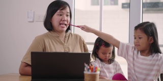 亚洲妇女视频通话笔记本电脑，同时照顾她的女儿在家里