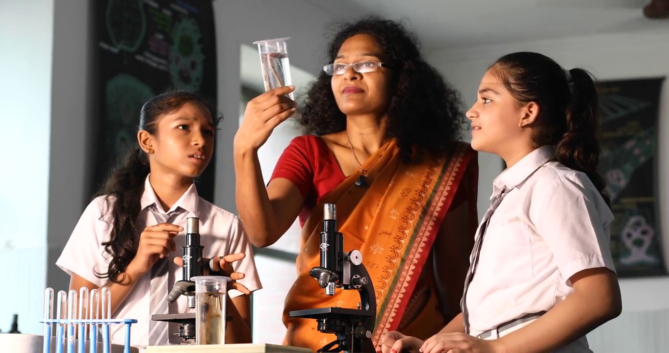 两名女学生跟着老师用显微镜进行实验室实验