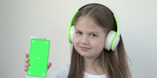 漂亮的白人女孩在大无线耳机显示手机与绿色屏幕模拟