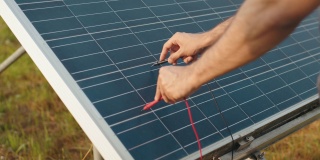男性的手在户外用万用表检查太阳能电池板的电压的特写。能胜任太阳能电站的控制工作。用万用表检查太阳能板电压